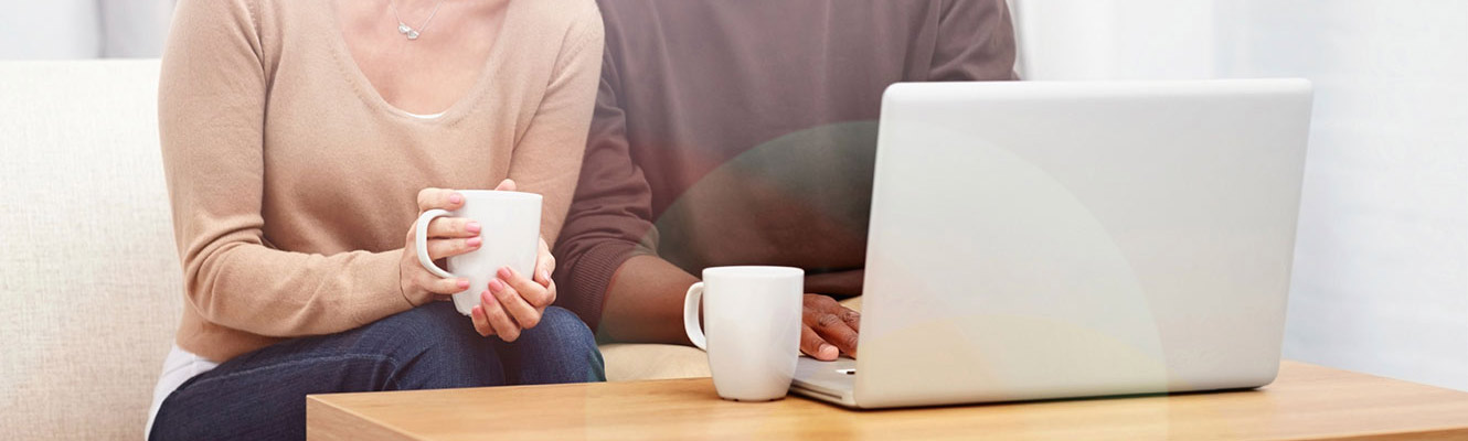 Adult couple having coffee at home, on laptop.