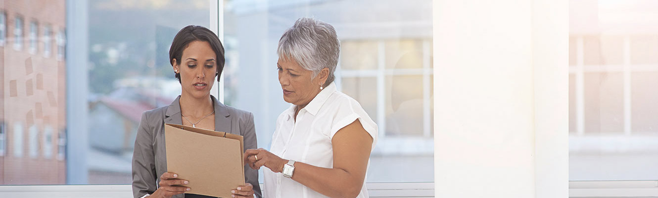 Two woman in business office discussing paperwork.