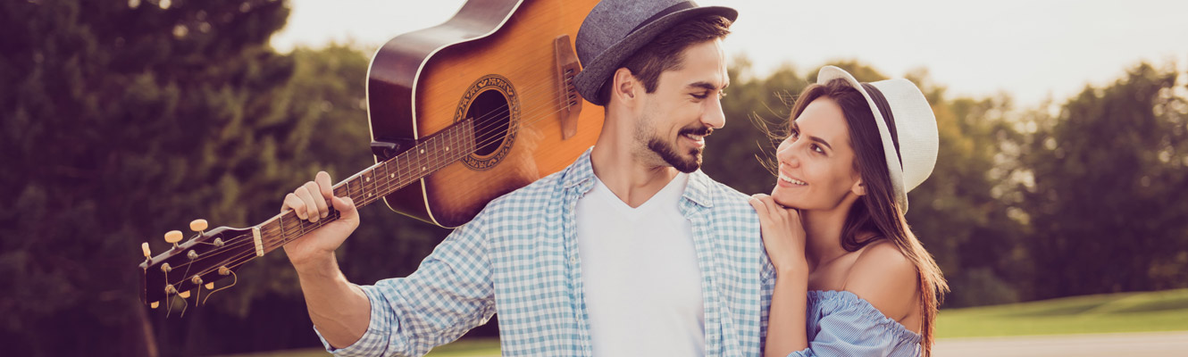 Man with guitar on shoulder and woman leaning on him in a park-like setting