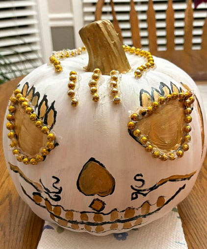 Pumpkin entry #4 - white pumpkin with gold jewels outlining the top of the pumpkin and her gold eyes. Nose is an upside down heart shape in gold and it has gold teeth.