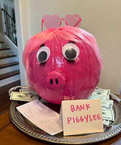 Pumpkin decorating entry #11 named Bank Piggysee - pink pumpkin with heart-shaped glasses, big eyes on. a plate of money